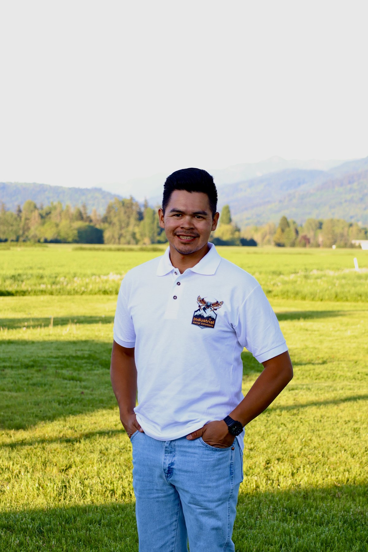 Dion Archie, founder and pilot of Industrial Aerial Solutions, standing in a green Fraser Valley field with mountains behind him
